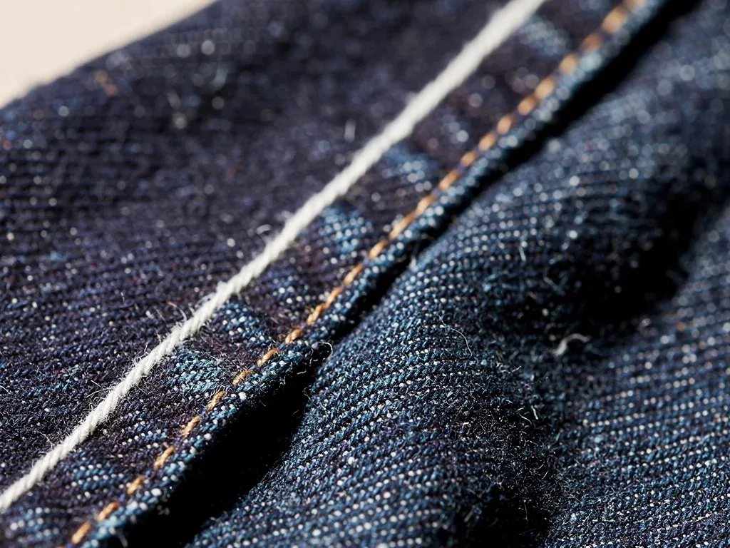 Close-up of high-quality raw denim fabric with a selvedge edge, emphasizing texture and color.